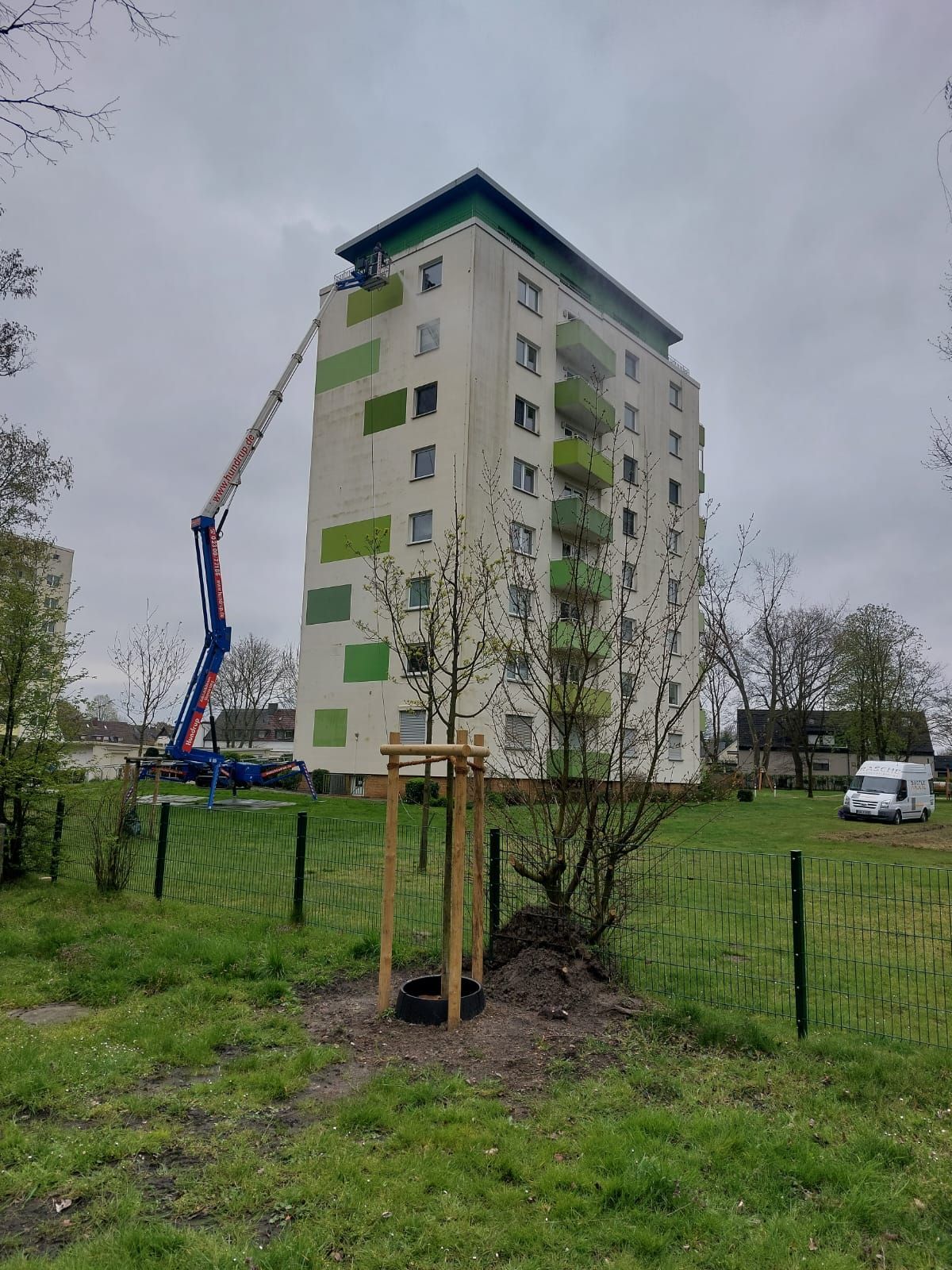 Ein hohes Gebäude mit einem Kran darauf und einem Baum davor.