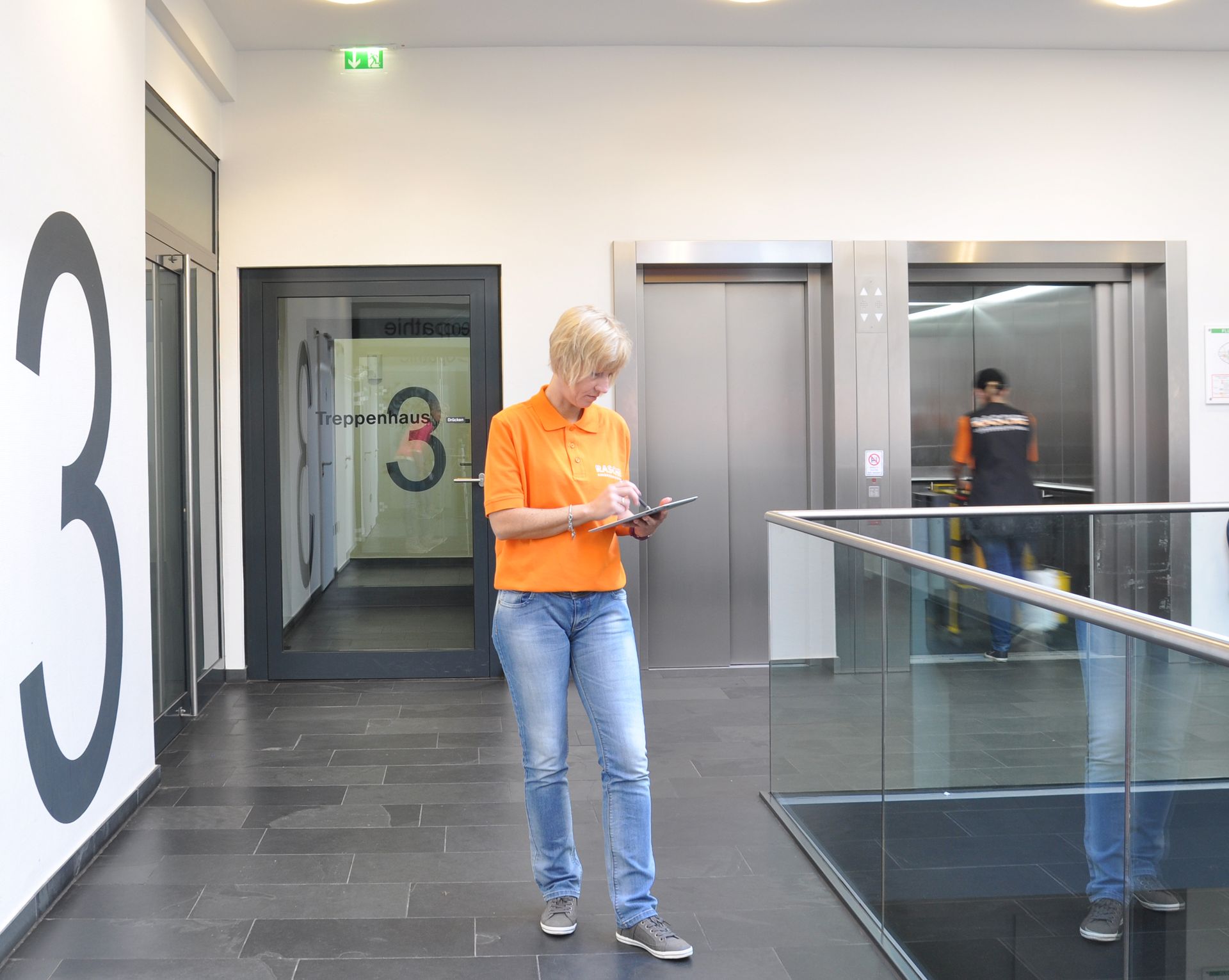 Ein Mann reinigt die Fassade eines dreieckigen Gebäudes mithilfe eines Krans.