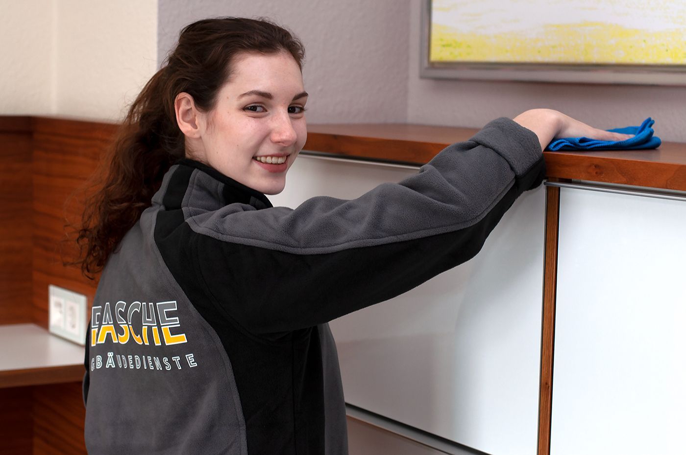 Eine Frau reinigt einen Schrank mit einem Tuch und lächelt.