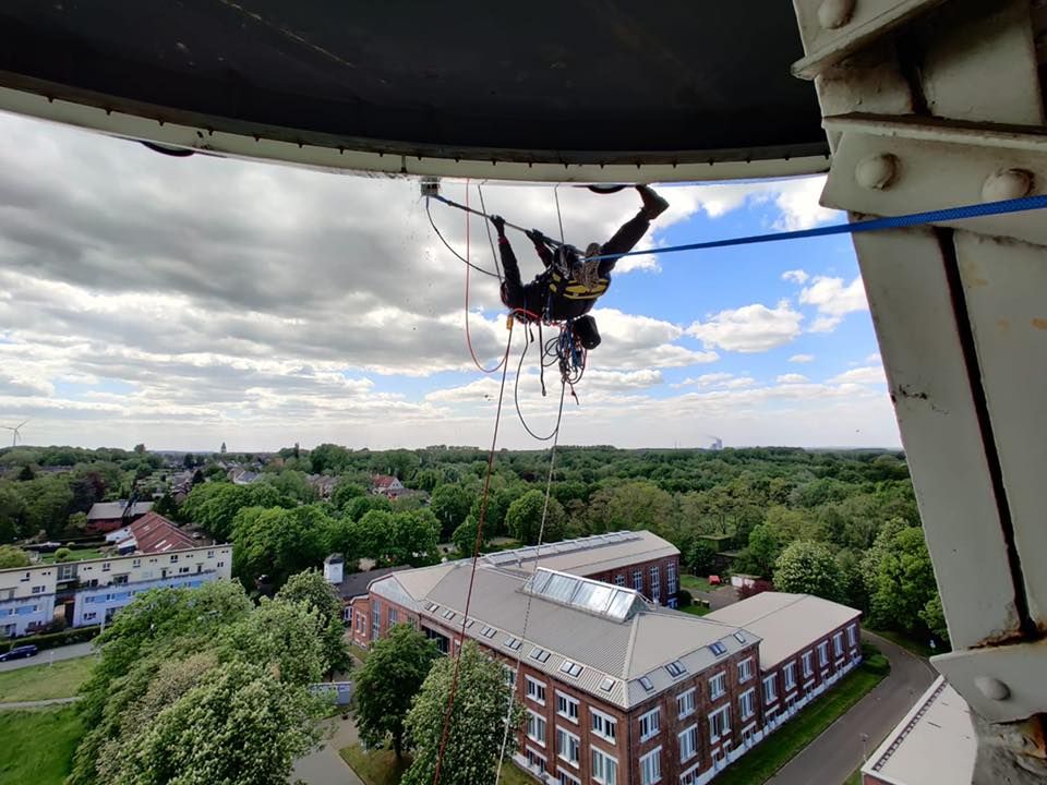 Ein Mann reinigt die Fassade eines dreieckigen Gebäudes mithilfe eines Krans.