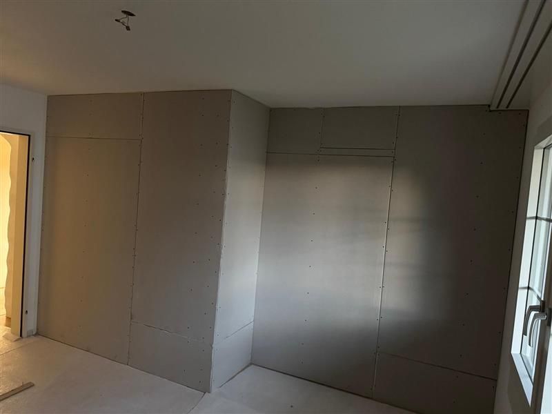 Ein Zimmer mit Holzboden und vielen Fenstern wird umgebaut.