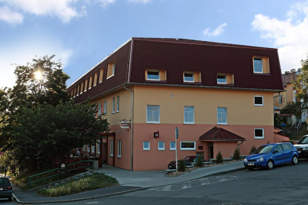 Gelb-lachsfarbenes Gebäude mit braunem Dach. Straße davor, blaues Auto geparkt.