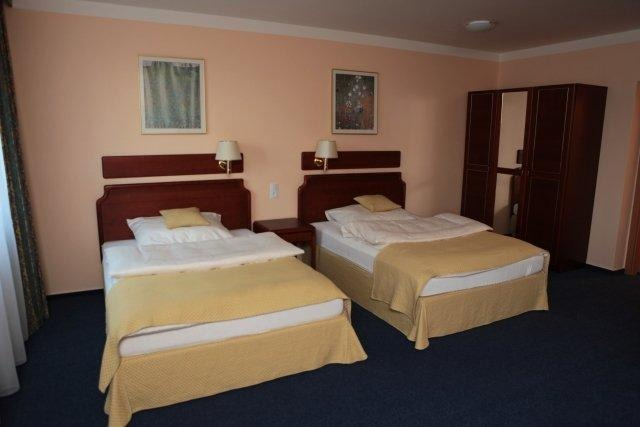 Hotelzimmer mit zwei Einzelbetten, Nachttischen, Kleiderschrank, Kunstwerken und hellbraunen Wänden.