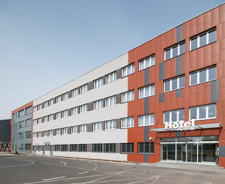 Die Hotelfassade ist mit grauen, roten und weißen Paneelen verkleidet. Der Eingang verfügt über Glastüren unter dem Hotelnamen.