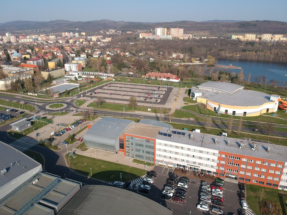 Luftaufnahme von Gebäuden, Parkplätzen und einem See in einer Stadt mit Bäumen und Hügeln im Hintergrund.