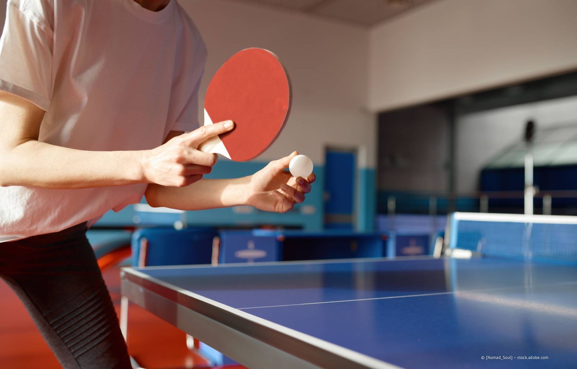 Eine Person bereitet sich darauf vor, mit einem roten Schläger einen Tischtennisball über einen blauen Tisch zu schlagen.