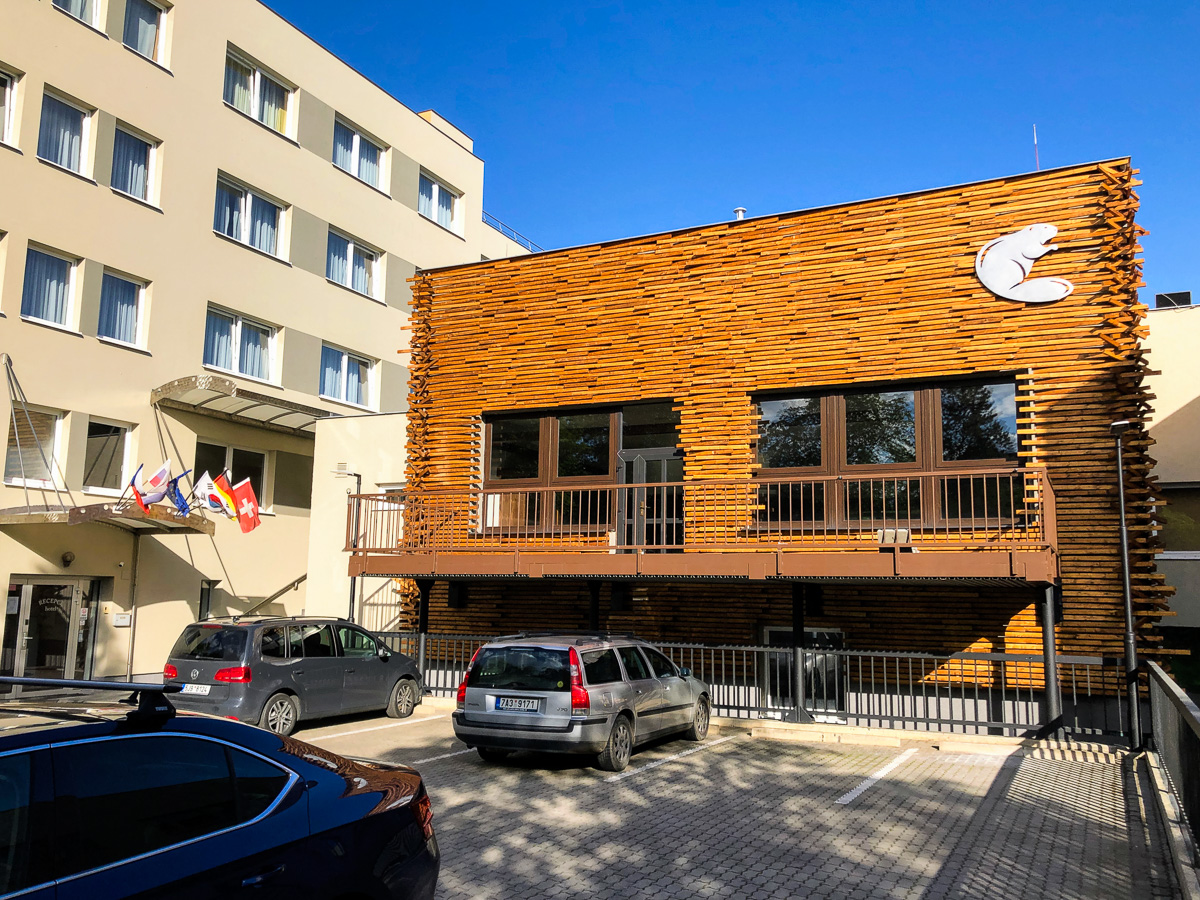 Ein Holzgebäude mit einem Halbmond-Logo steht neben einem beigen Wohnhaus. Davor parken Autos.