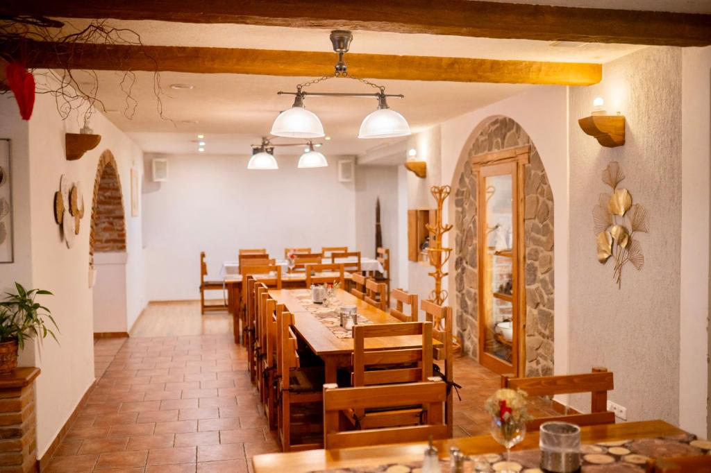 Speisesaal mit langen Holztischen, Stühlen, Bogentüren und Pendelleuchten.
