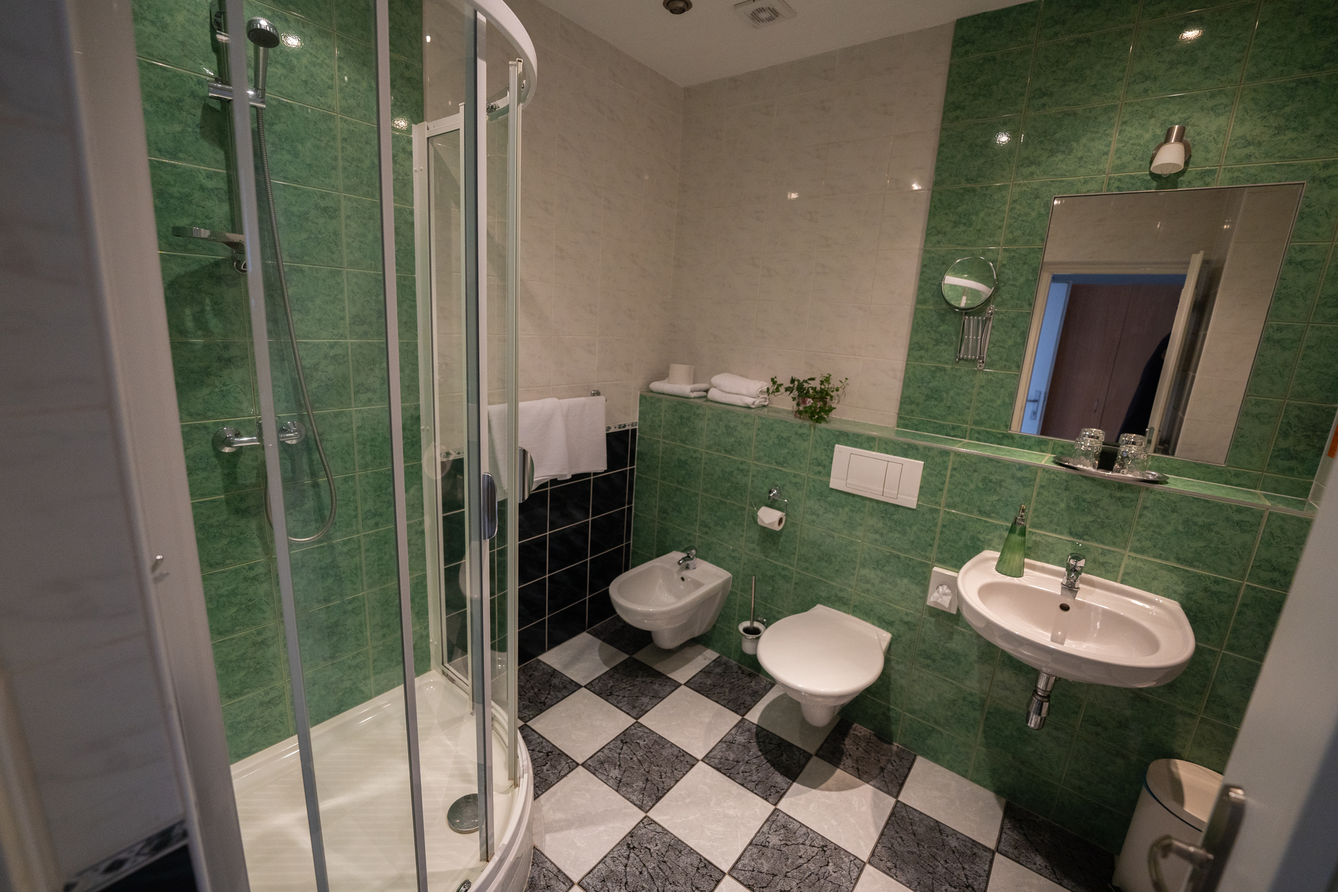 Badezimmer mit grünen Fliesenwänden, Schachbrettboden, Dusche, Toilette und Waschbecken.