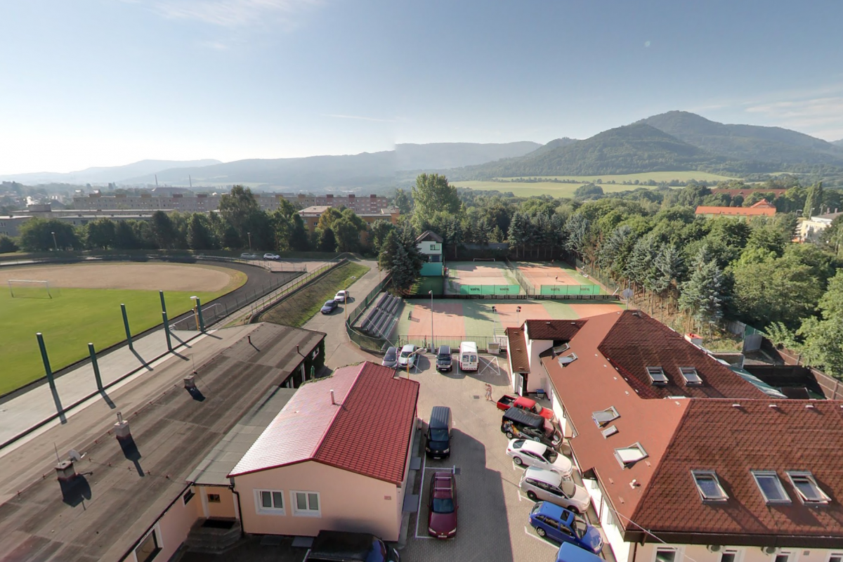 Luftaufnahme eines Sportkomplexes mit Tennisplätzen, Stadion, Gebäuden und Bergen in der Ferne.