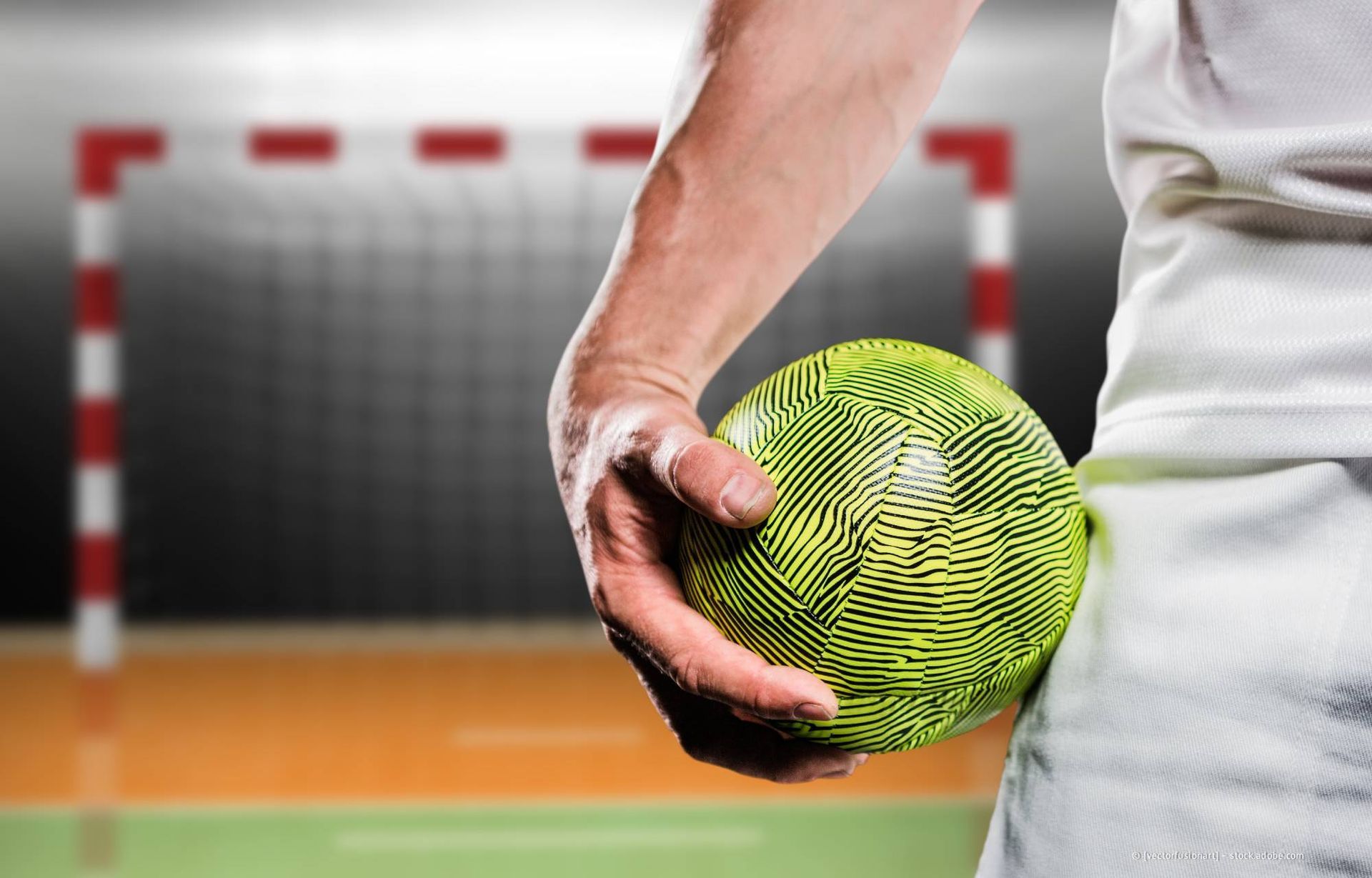 Eine Frau will im Handballspiel einen gelben Ball werfen, eine andere Frau steht im Tor. Draußen, sonnig.
