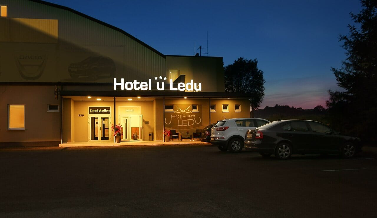 Hotel U Ledu in der Abenddämmerung mit beleuchtetem Schild, Eingang und davor geparkten Autos.