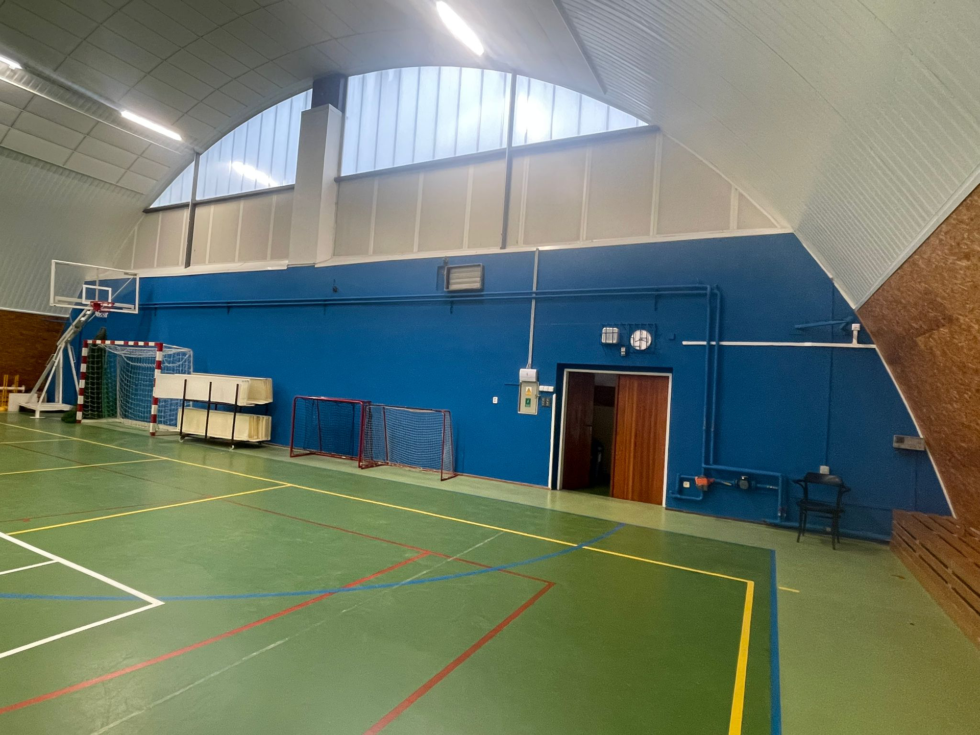 Sporthalle mit blauer Wand, gewölbter Decke, Sportgeräten und Holztür.
