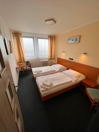 Hotelzimmer mit zwei Einzelbetten, Nachttischen und einem Fenster mit Vorhängen. Dunkler Teppich.