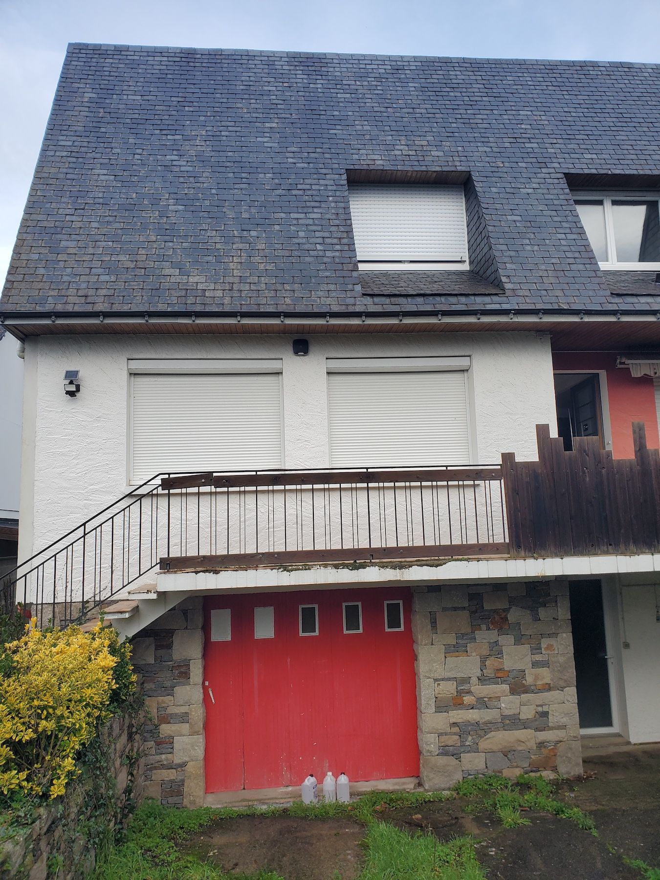 Maison à deux étages avec une porte de garage rouge, des volets blancs et un toit en ardoise foncée