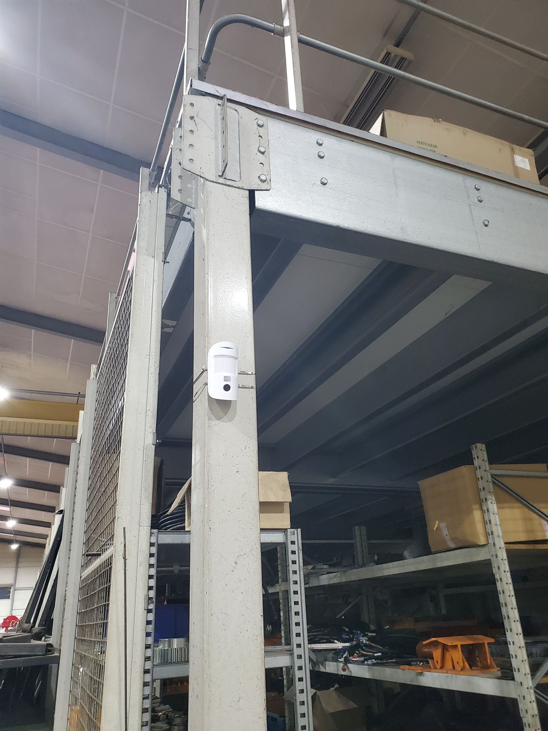 Étagère d'entrepôt avec montants métalliques, un capteur blanc et des cartons empilés sur une plateforme supérieure