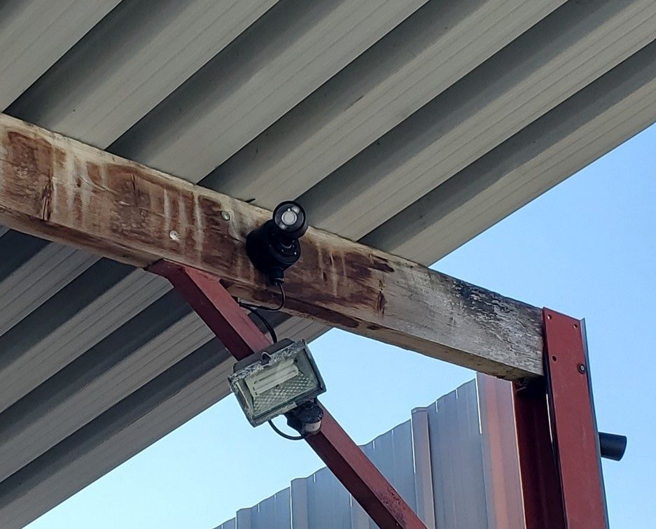 Caméra de vidéosurveillance fixée sur une poutre en acier rouillée sous un toit en tôle ondulée