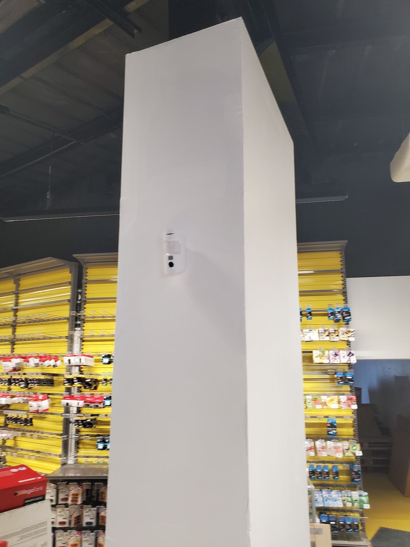 Présentoir vertical blanc de grande taille dans une allée de magasin, avec des étagères de produits jaunes en arrière-plan.