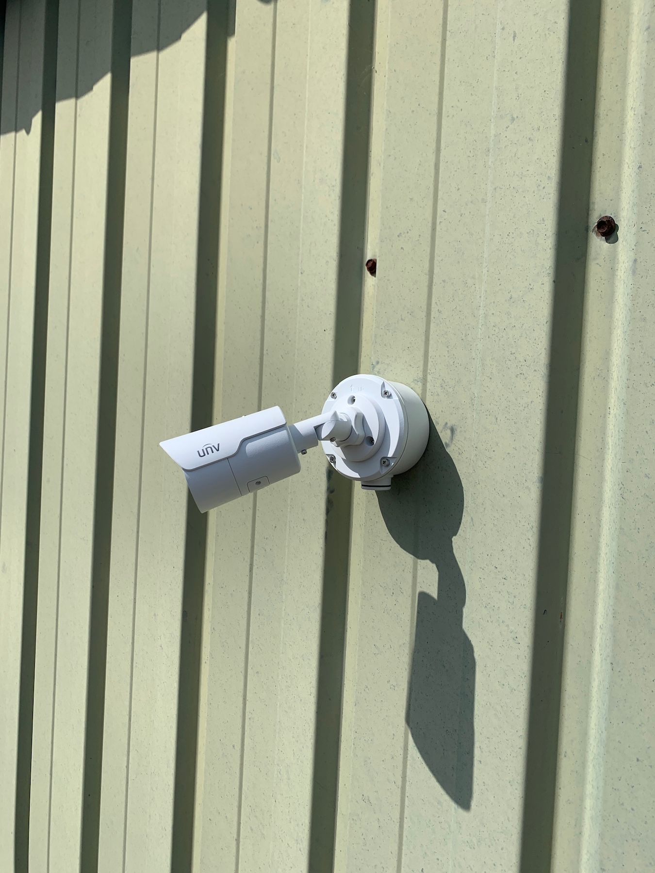 Caméra de sécurité fixée sur un mur vert pâle, projetant une longue ombre.