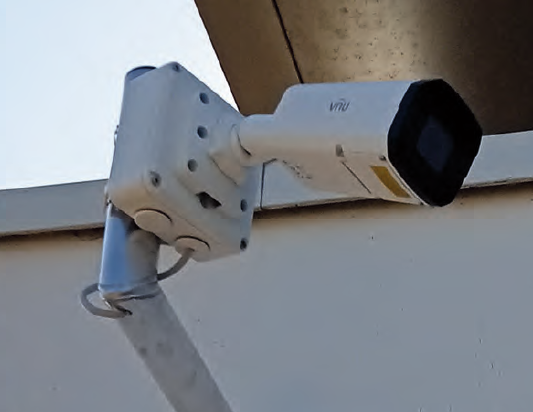 Caméra de sécurité blanche fixée sous un avant-toit, inclinée vers le bas.