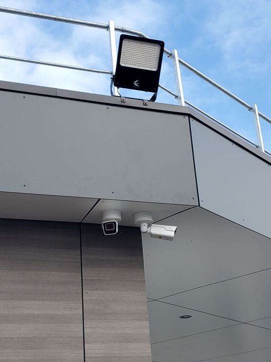 Coin d'un bâtiment avec projecteur sur le toit, caméra de sécurité et caméra de surveillance blanche sous un ciel nuageux