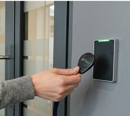 Main tenant un porte-clés électronique près d'un lecteur d'accès mural noir avec un voyant vert