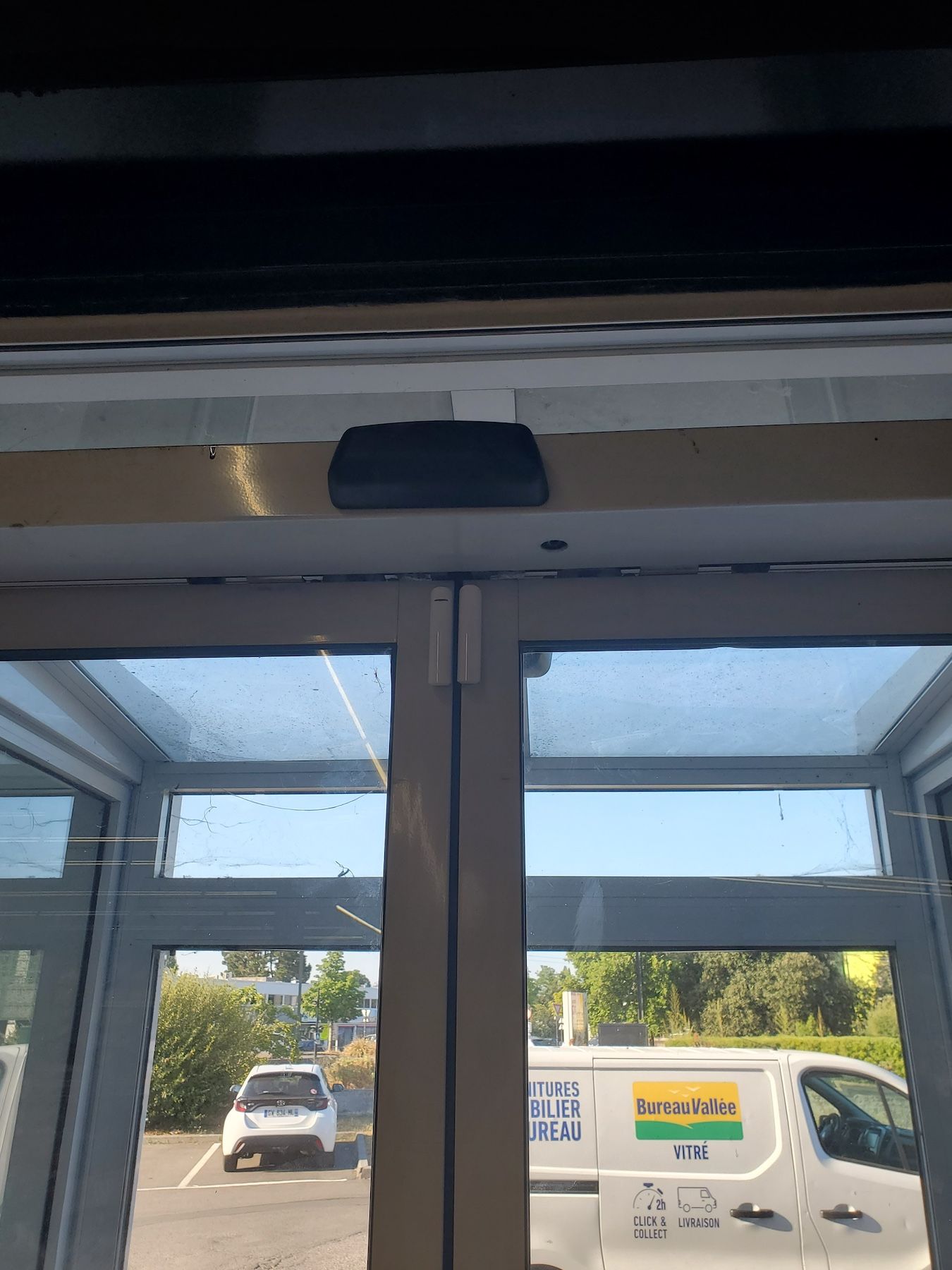 Vue à travers les portes vitrées d'un parking avec une camionnette blanche et la lumière vive du jour à l'extérieur