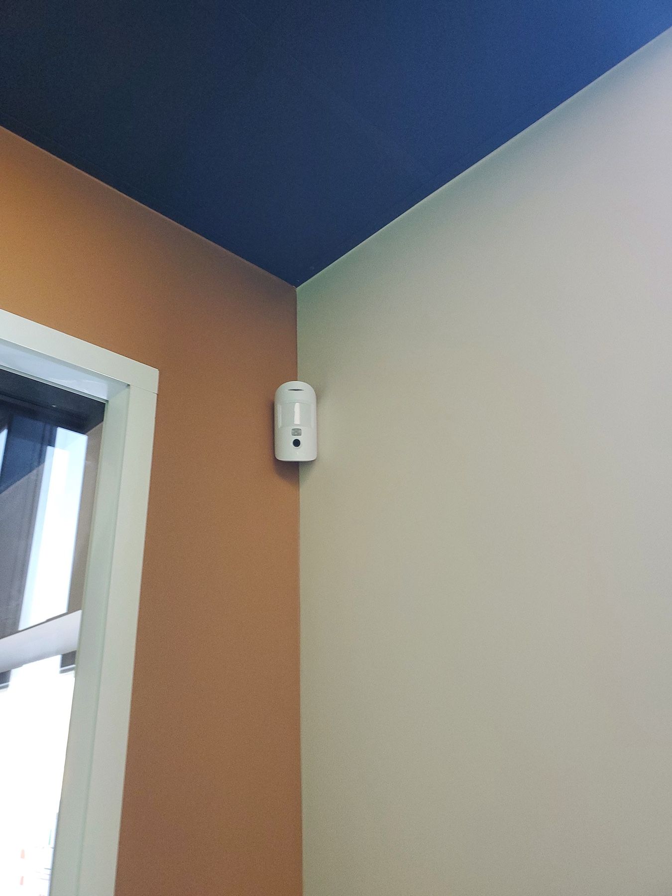Coin d'une pièce aux murs beiges et orange, au plafond bleu et avec une fenêtre sur la gauche.