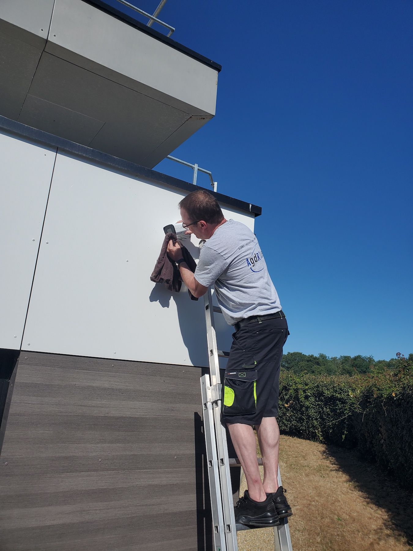 Une personne debout sur une échelle peint le côté d'une maison sous un ciel bleu clair