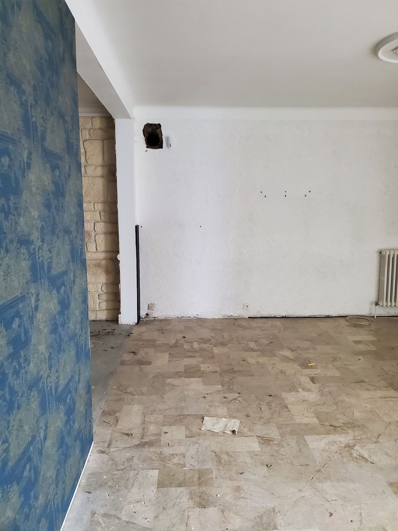 Pièce vide aux murs blancs, un mur texturé bleu et un sol carrelé usé.