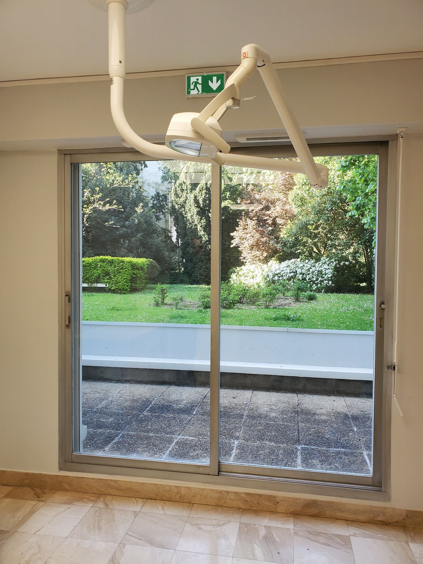 Porte coulissante en verre avec un tuyau blanc cassé au-dessus, donnant sur une allée de jardin et de la verdure.