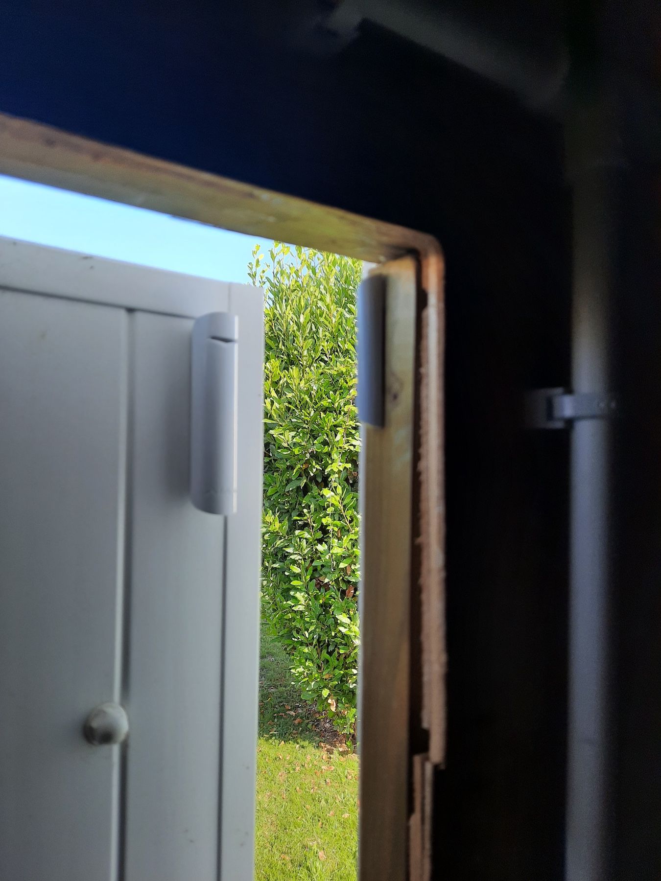 Porte entrouverte donnant sur une clôture blanche et un jardin vert.