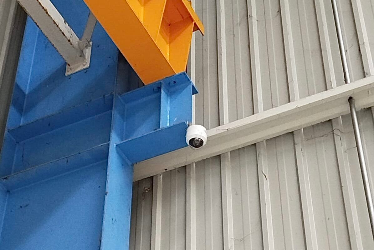 Caméra de sécurité blanche fixée sur une poutre bleue à côté d'un mur en tôle ondulée