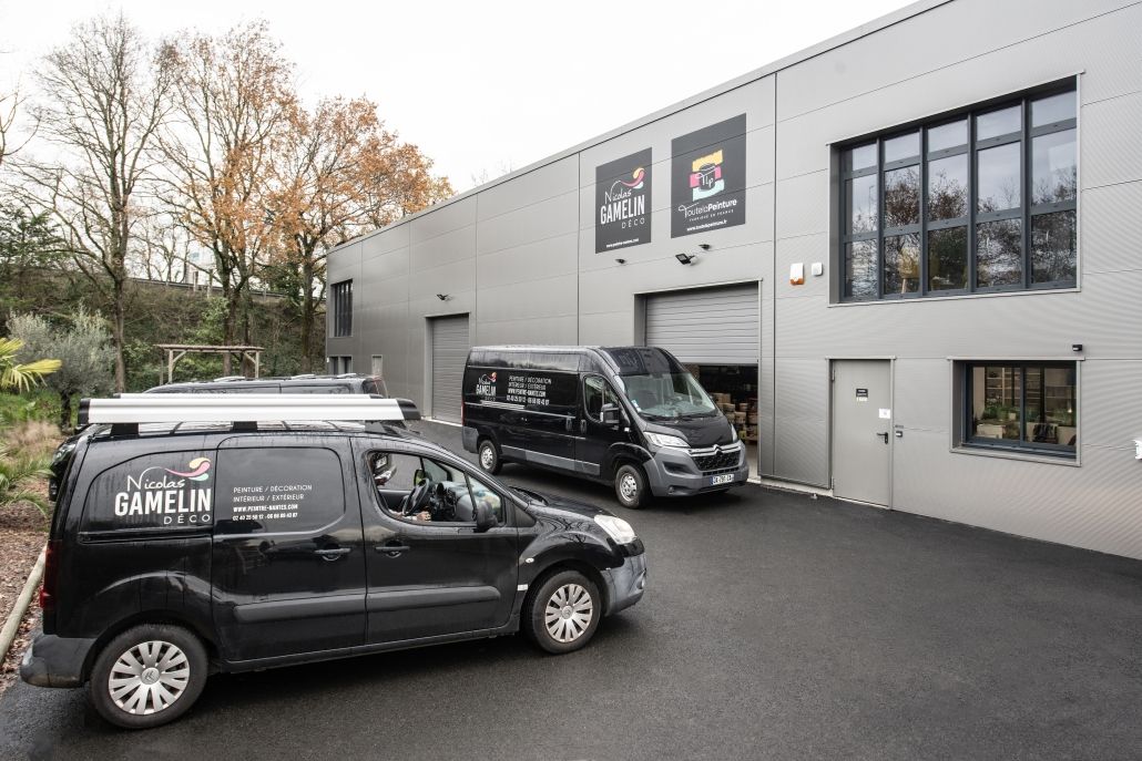 Deux fourgonnettes de service noires étaient garées devant un bâtiment industriel gris aux grandes fenêtres.
