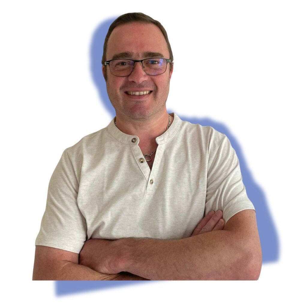 Homme souriant portant des lunettes et les bras croisés, vêtu d'une chemise blanche sur fond uni.