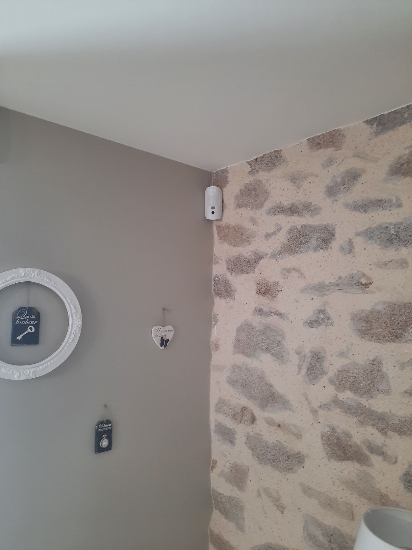 Coin d'une pièce aux murs gris à motifs de pierre, un miroir rond et un petit objet de décoration murale.