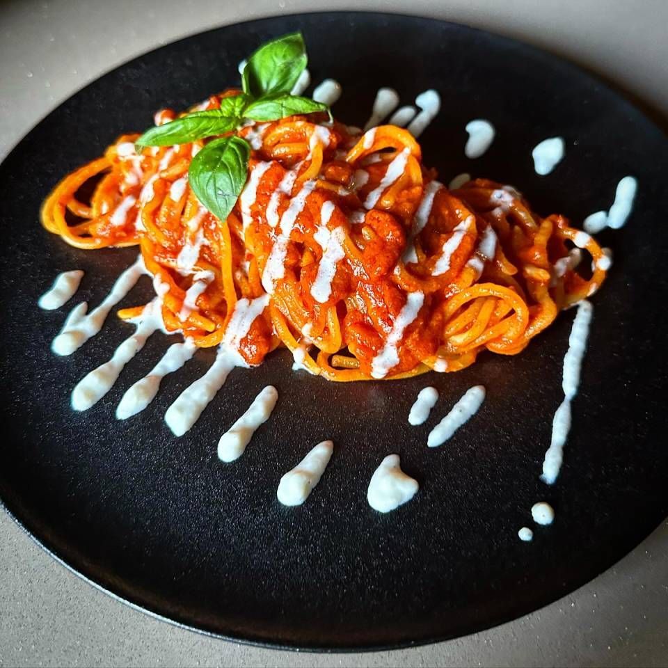 Une assiette noire garnie de spaghettis à la sauce et au basilic