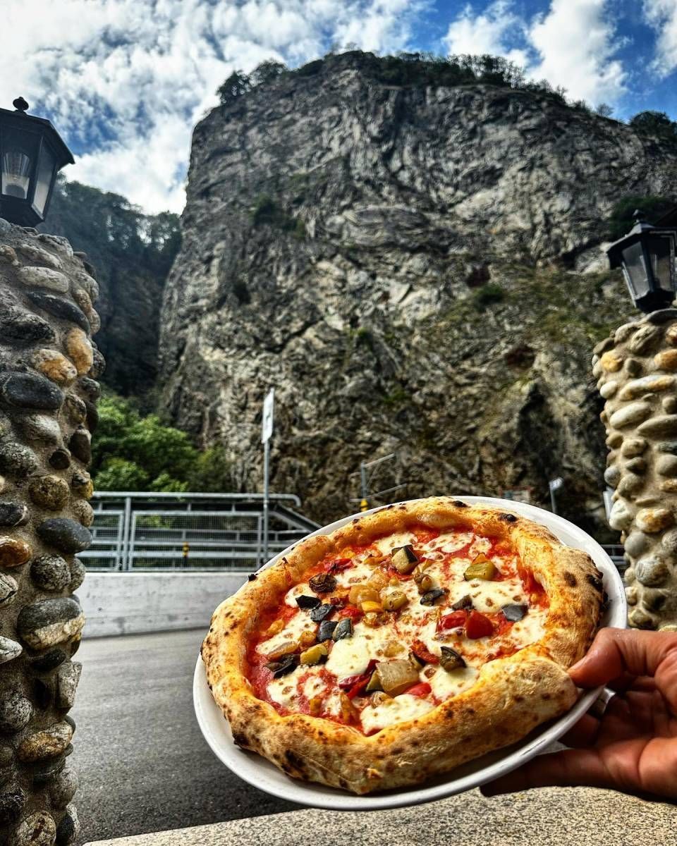 Une personne tient une pizza dans une assiette devant une montagne