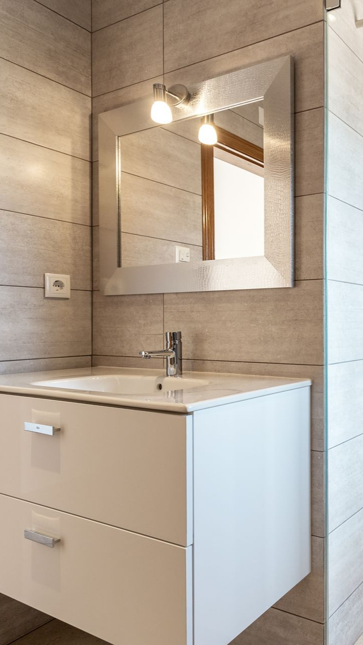 Salle de bains moderne avec meuble-lavabo blanc, miroir carré et deux luminaires.