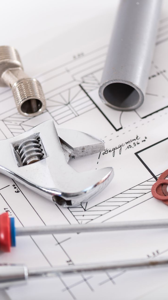 Outils de plomberie : clé, tuyau, raccords et plans disposés sur une surface.