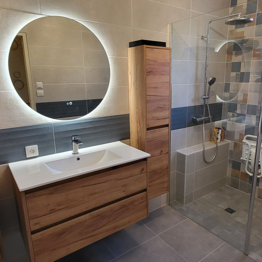 Salle de bains avec meuble-lavabo en bois, miroir rond rétroéclairé, douche et armoire de rangement haute.