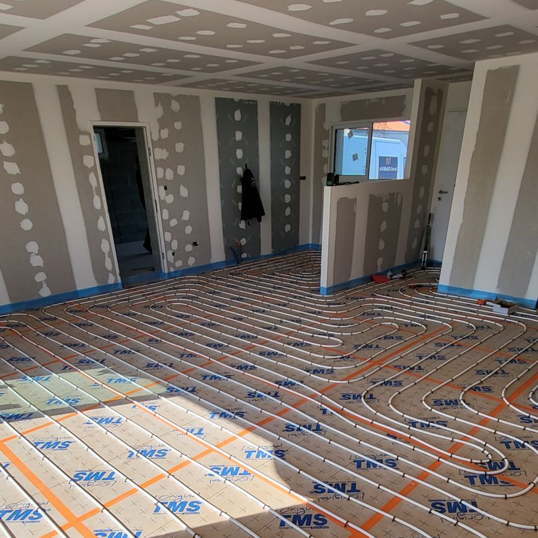 Pièce en construction avec système de chauffage au sol, murs en plaques de plâtre et porte ouverte.