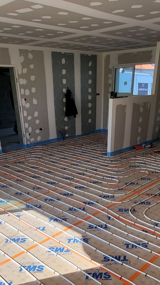 Une personne installe des tubes chauffants rouges sur une grille bleue, sur un plancher en bois.