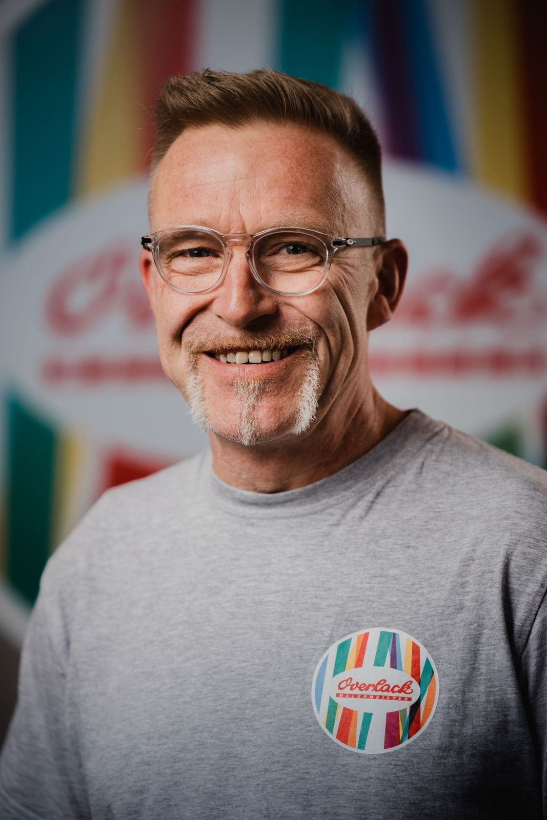 Ein Mann mit Brille und grauem Hemd lächelt in die Kamera.