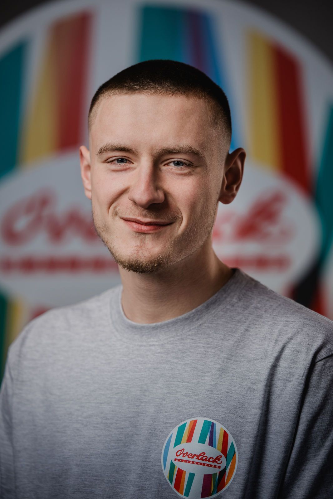 Ein junger Mann lächelt vor einem bunten Hintergrund.