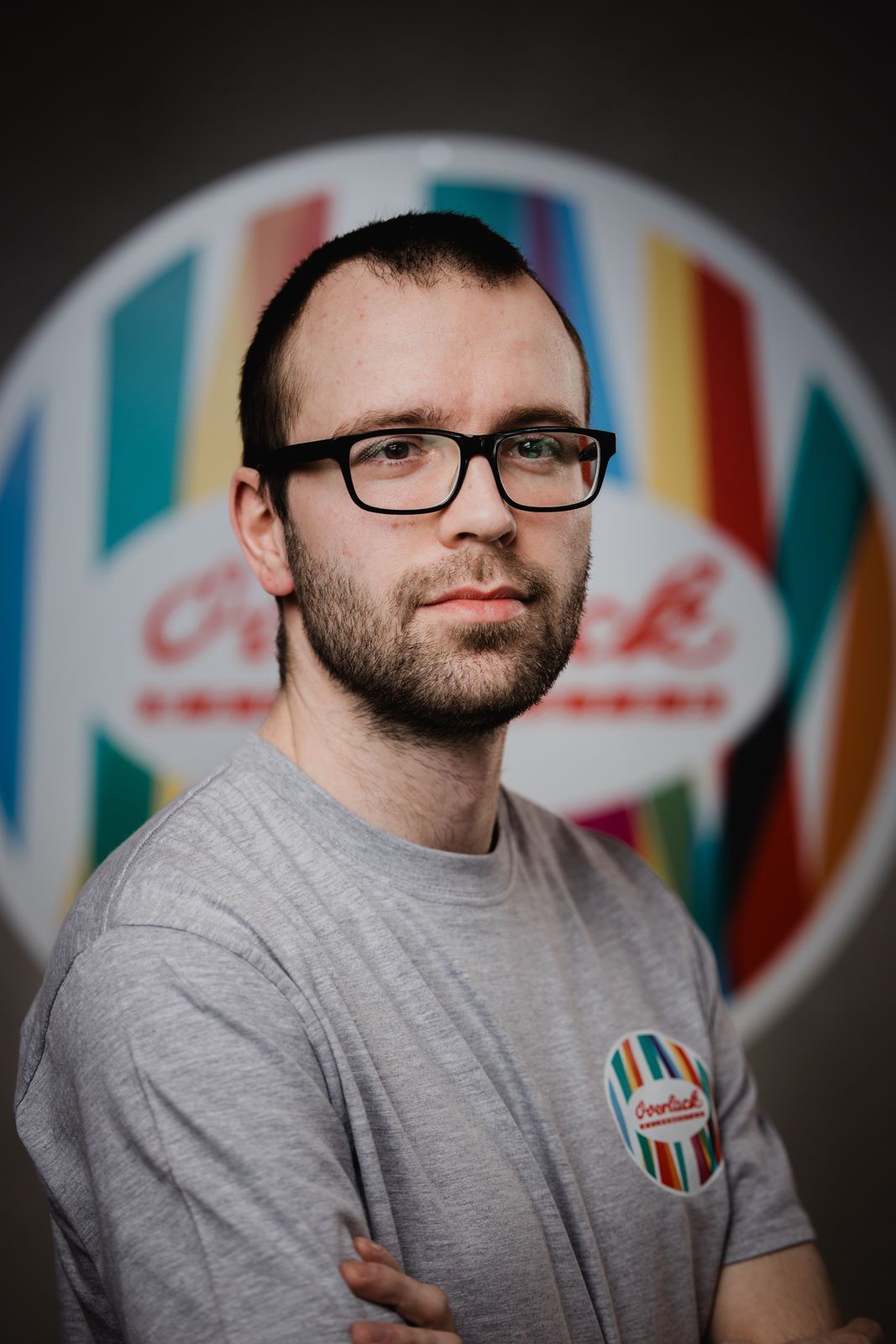 Ein Mann mit Brille und Bart steht vor einem bunten Schild.