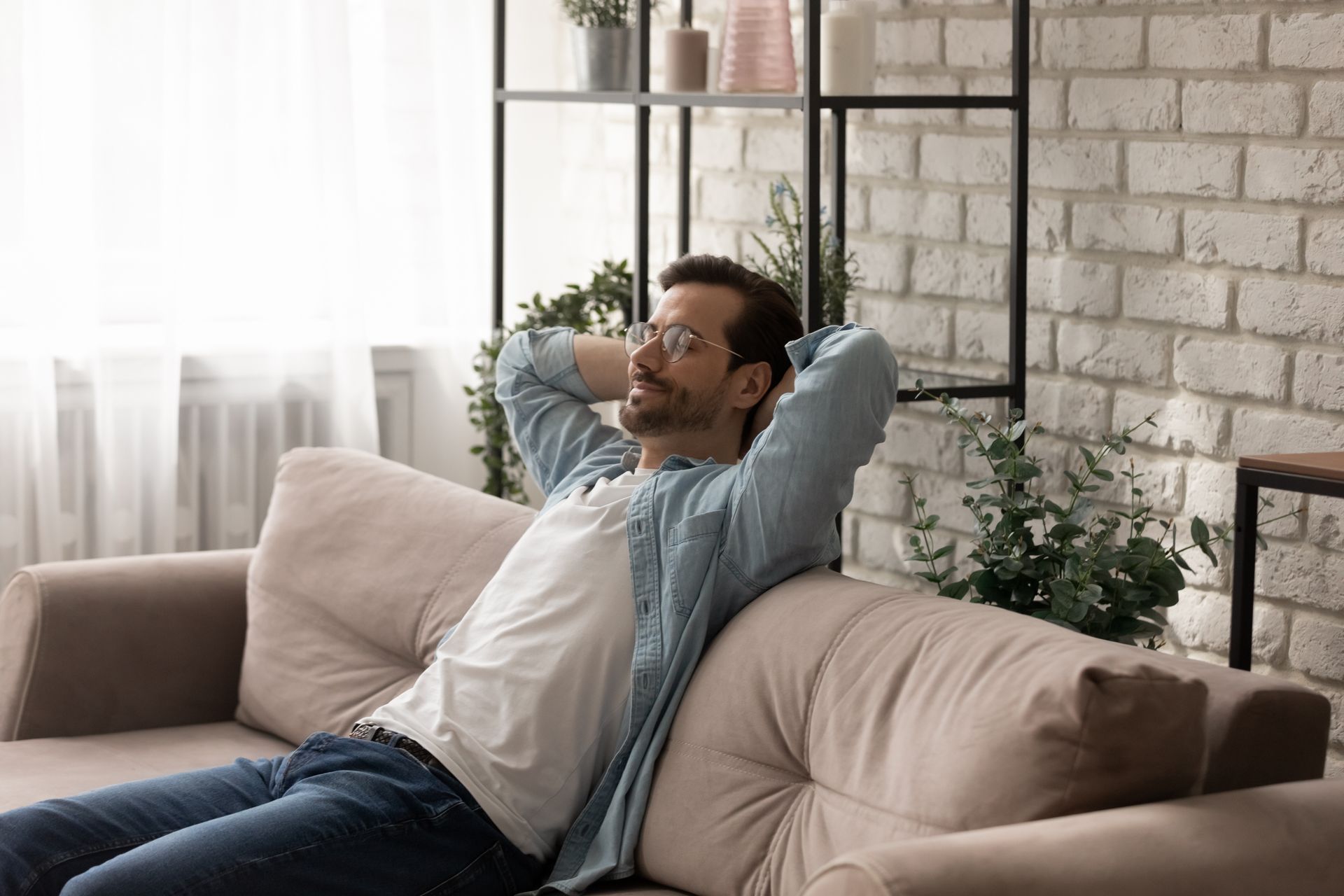Ein Mann sitzt mit den Händen hinter dem Kopf auf einem Sofa.