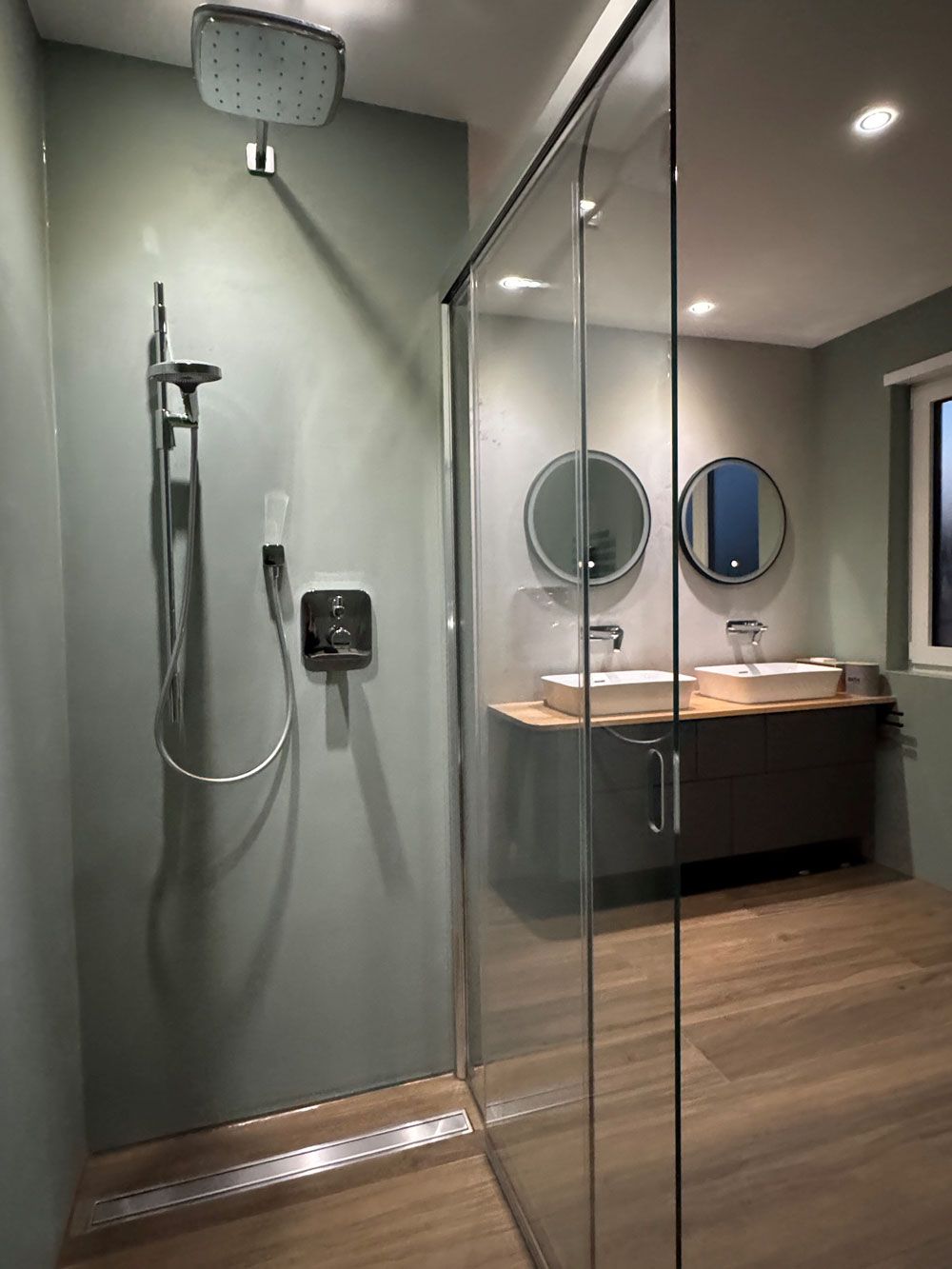 Ein Badezimmer mit Waschbecken, Spiegel und ebenerdiger Dusche.