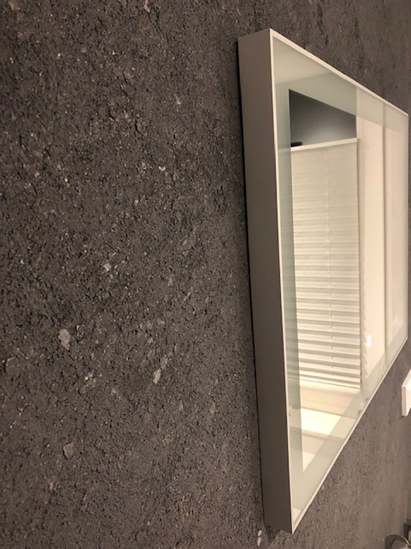 An einer grauen Wand hängt ein weißer Spiegel.