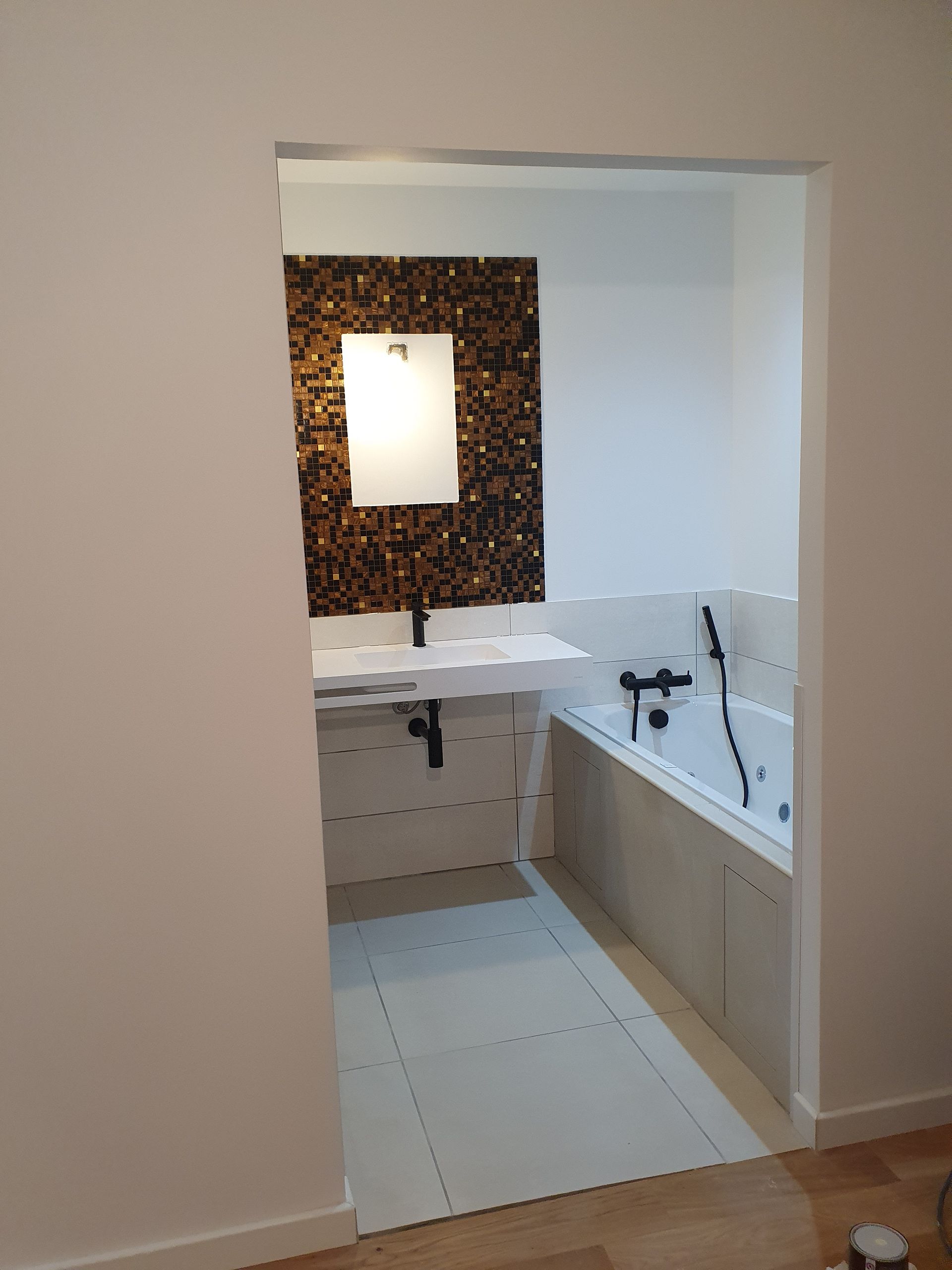 Salle de bains avec un mur d'accent en mosaïque, un lavabo blanc, une baignoire et des accessoires noirs.